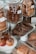 Assortment of baked goods displayed in a glass bakery case. Large glass jars contain stacks of cookies, including chocolate and oatmeal raisin varieties. Muffins with raisins are placed on a plate in the foreground, while croissants and pastries are arranged on wooden boards.