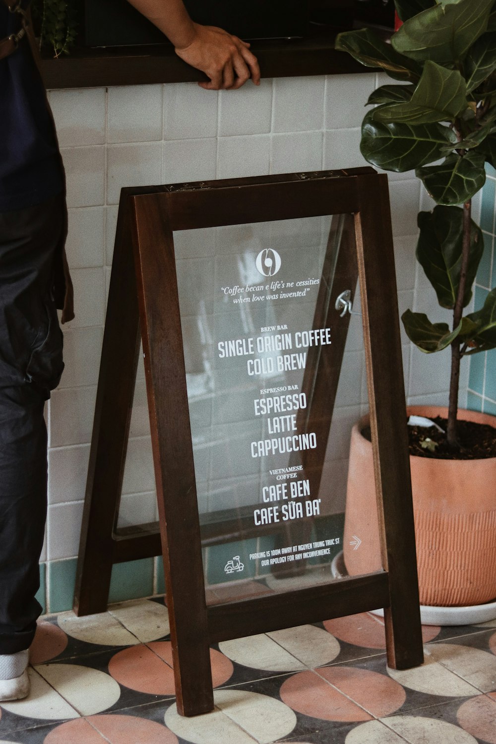 a person standing next to a sign in front of a potted plant