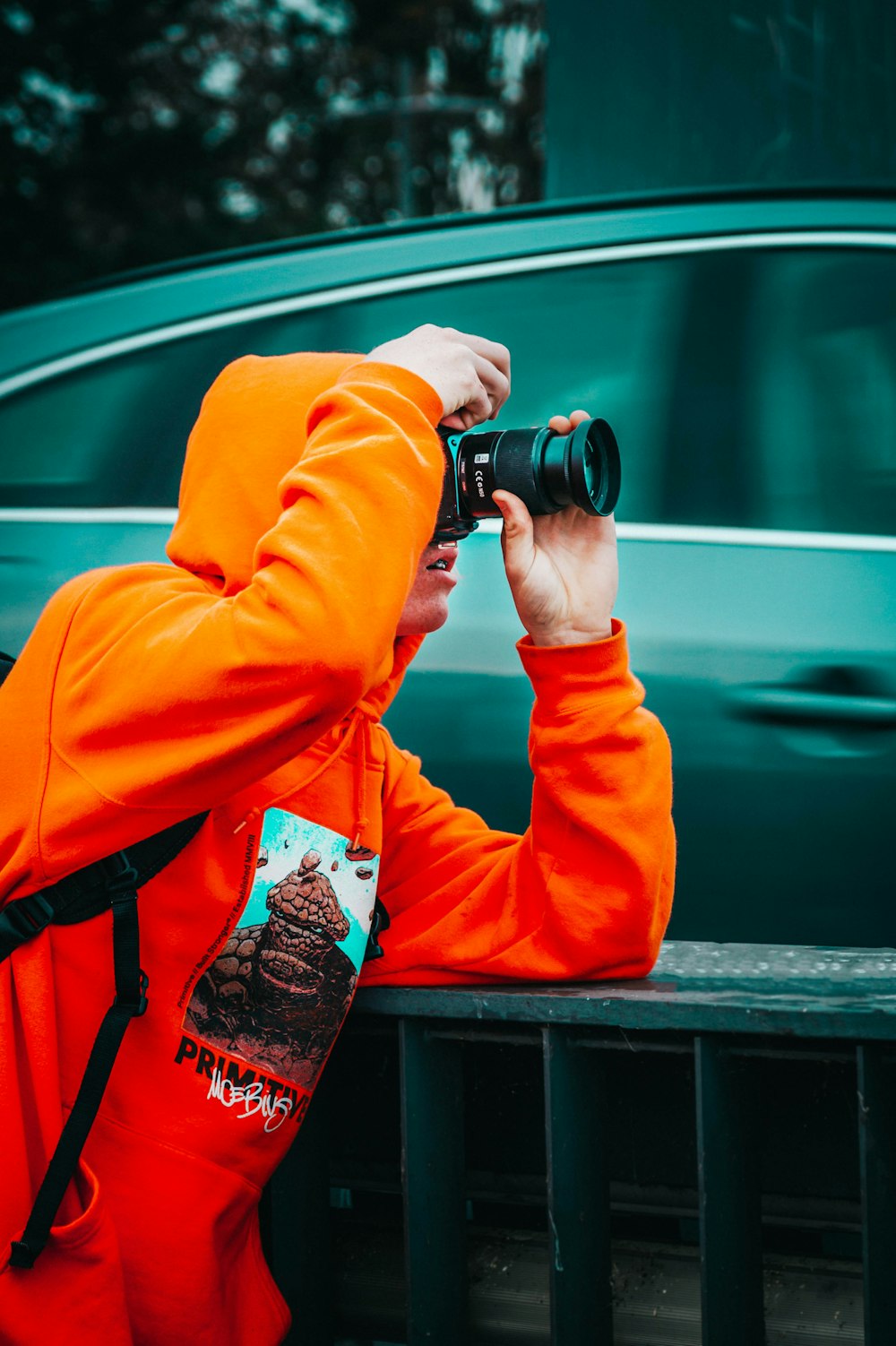 Un hombre con una sudadera con capucha naranja tomando una foto con una cámara