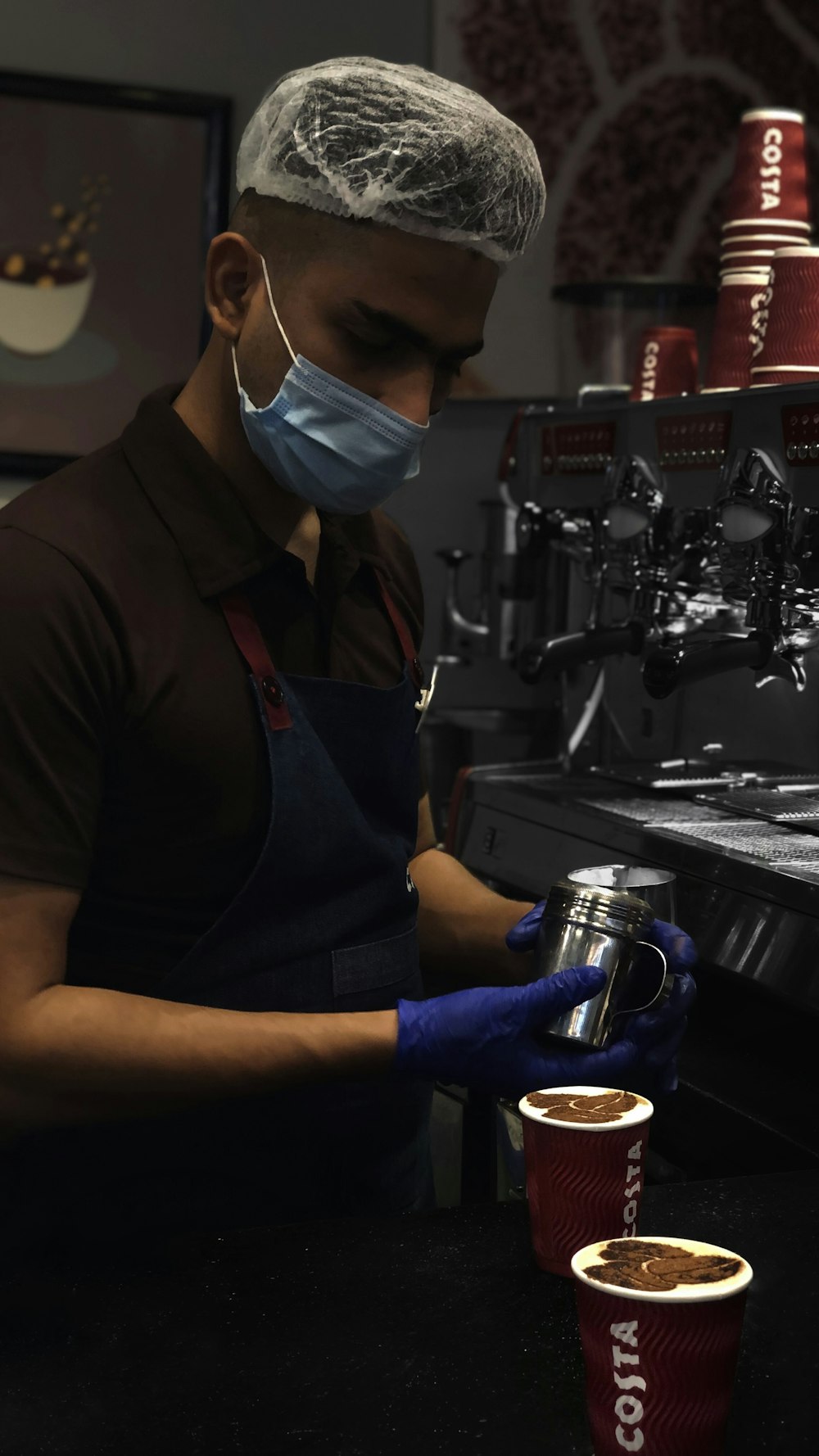 a man wearing a face mask and gloves pours a cup of coffee