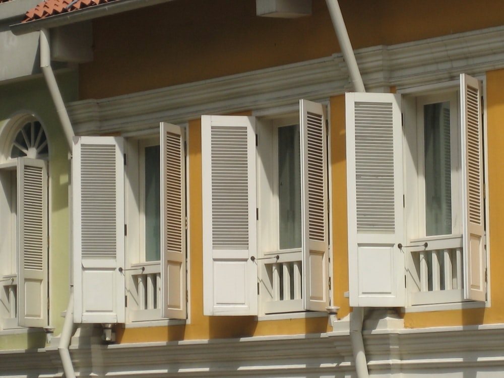 a row of white shutters on a yellow building