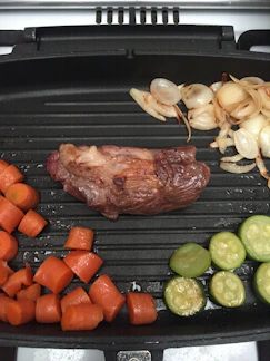 Close-up of a sleek stainless steel grill pan with fresh vegetables sizzling inside.