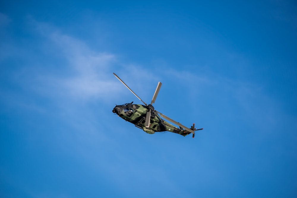 a military helicopter flying through a blue sky