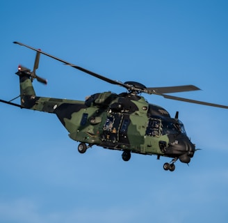 a military helicopter flying through a blue sky