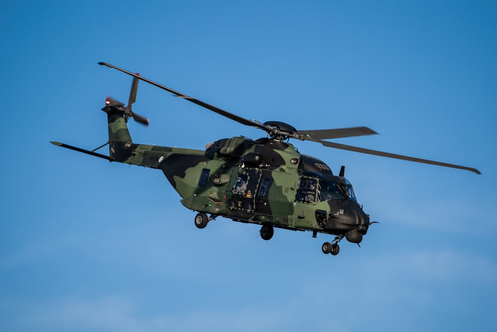 a military helicopter flying through a blue sky