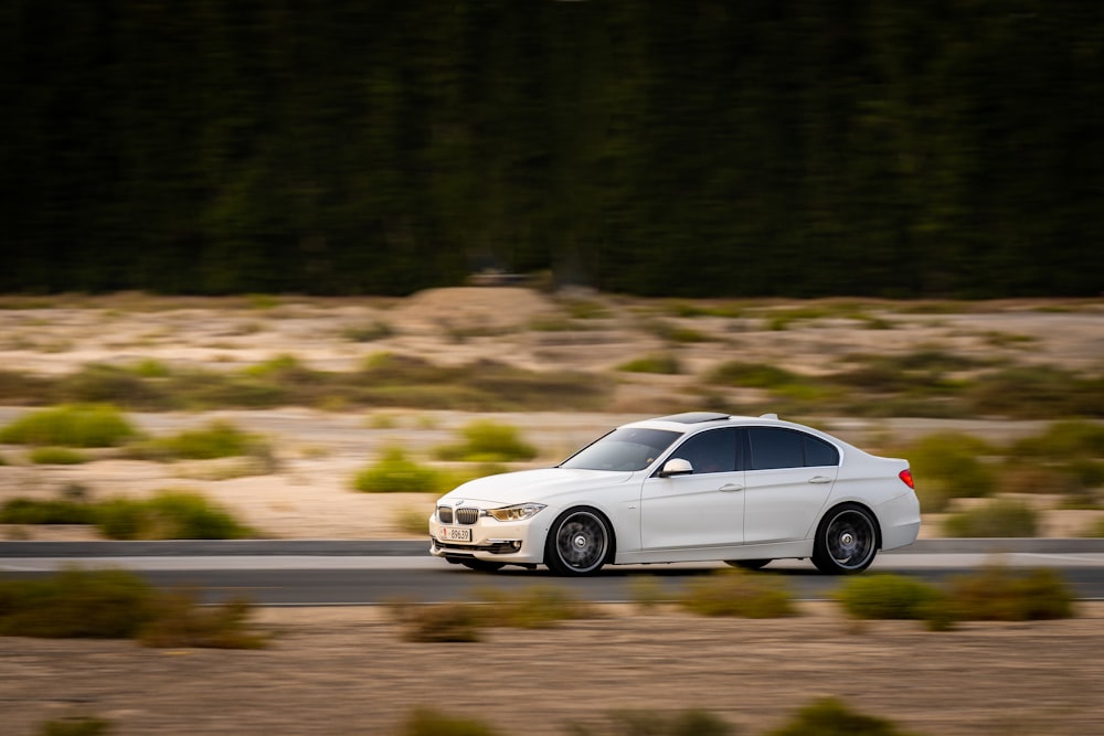 a white car driving down a road next to a forest