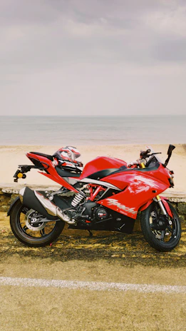 A shiny red sports motorcycle speeding along a coastal road.