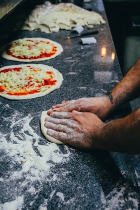 two uncooked pizzas sitting on top of a counter