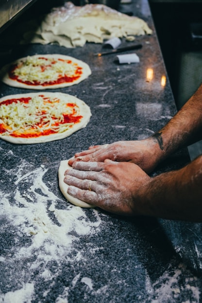 two uncooked pizzas sitting on top of a counter