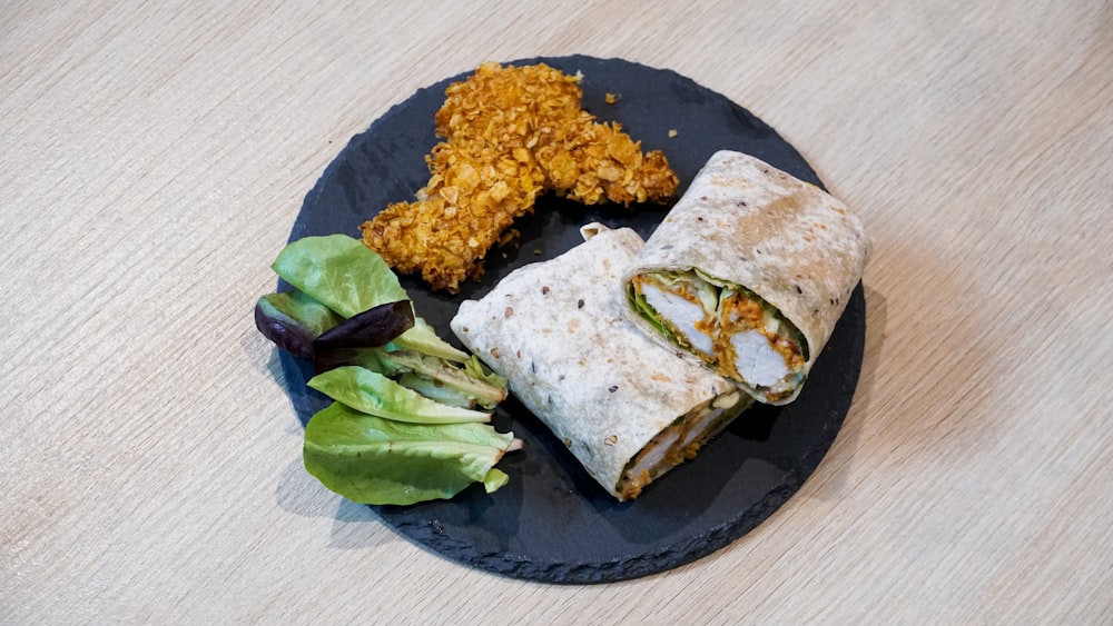 a black plate topped with a burrito and a salad