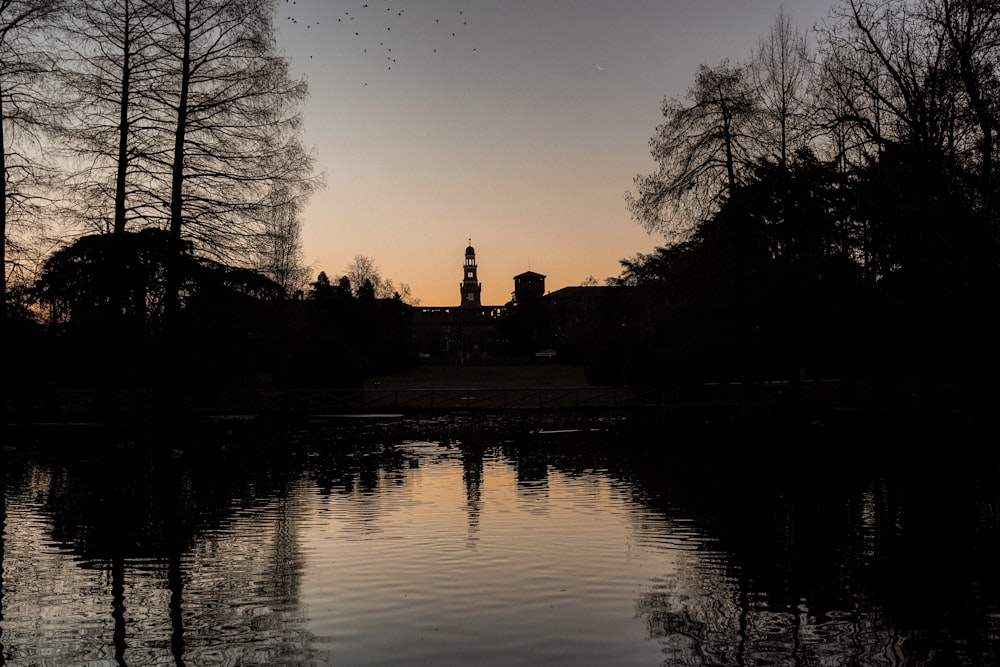 the sun is setting over a lake with a tower in the background