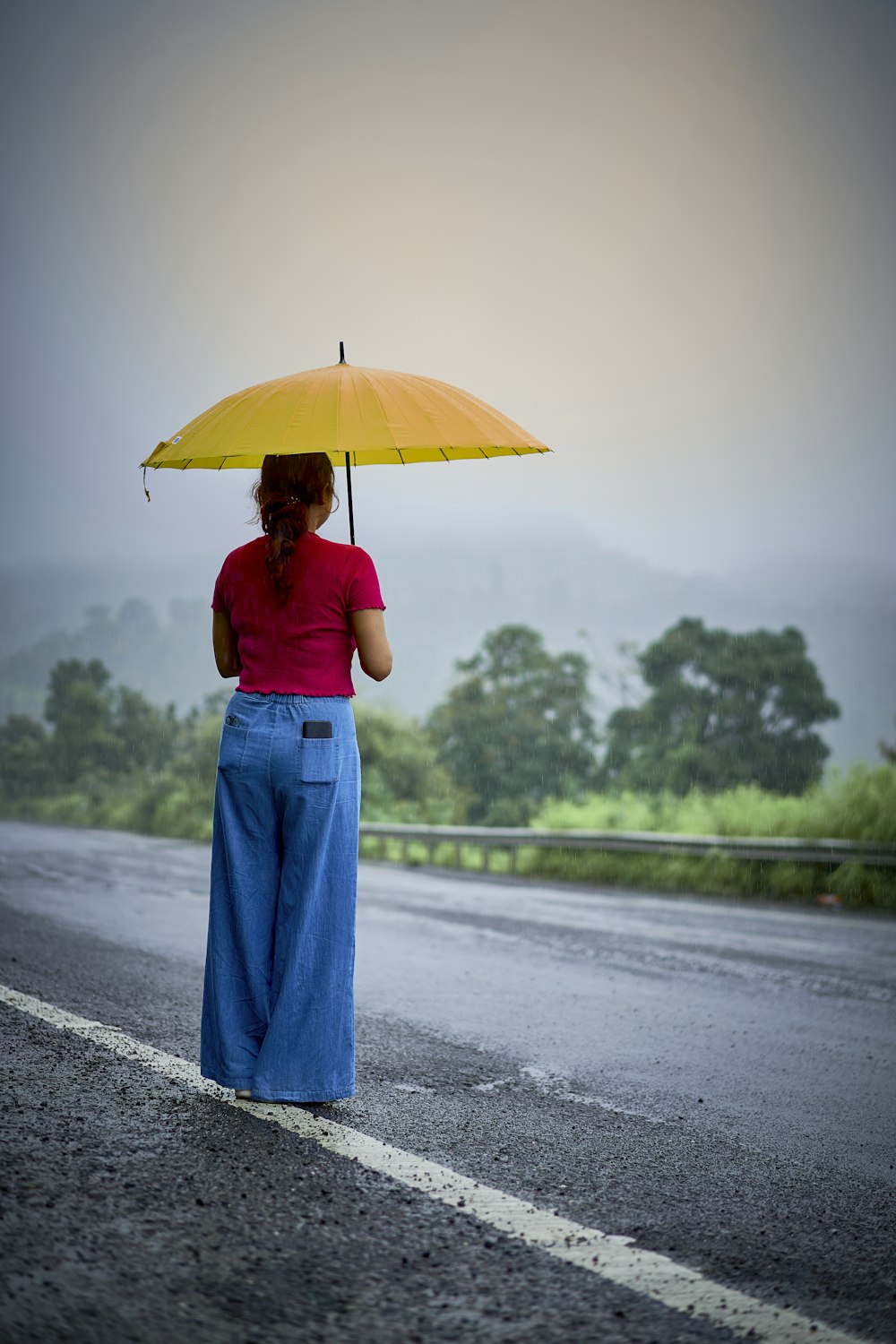 a woman holding an umbrella while standing on the side of a road