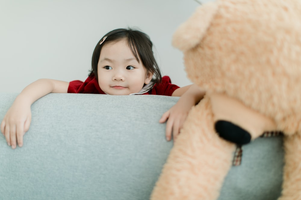 a little girl sitting on a couch next to a teddy bear