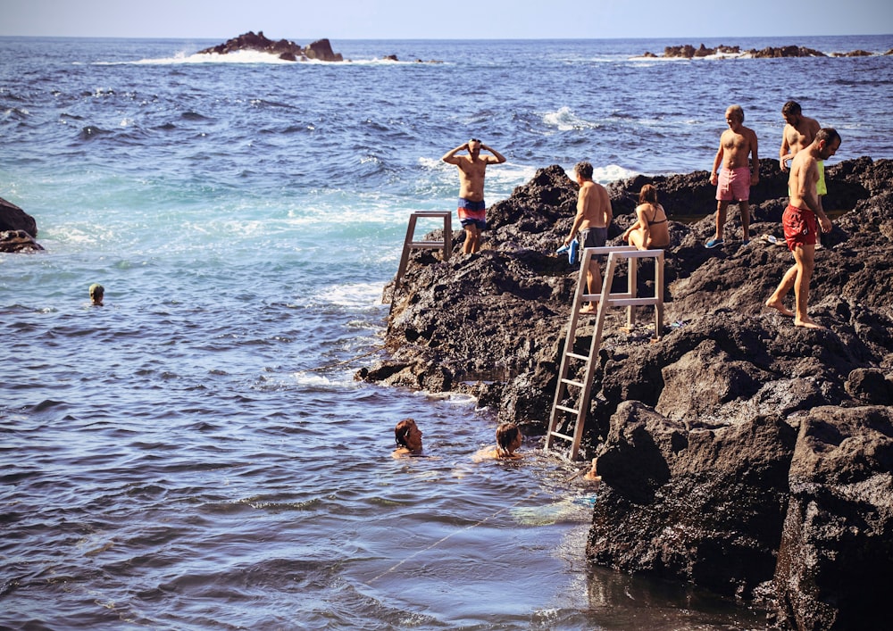a group of people standing on top of a rocky cliff next to the ocean