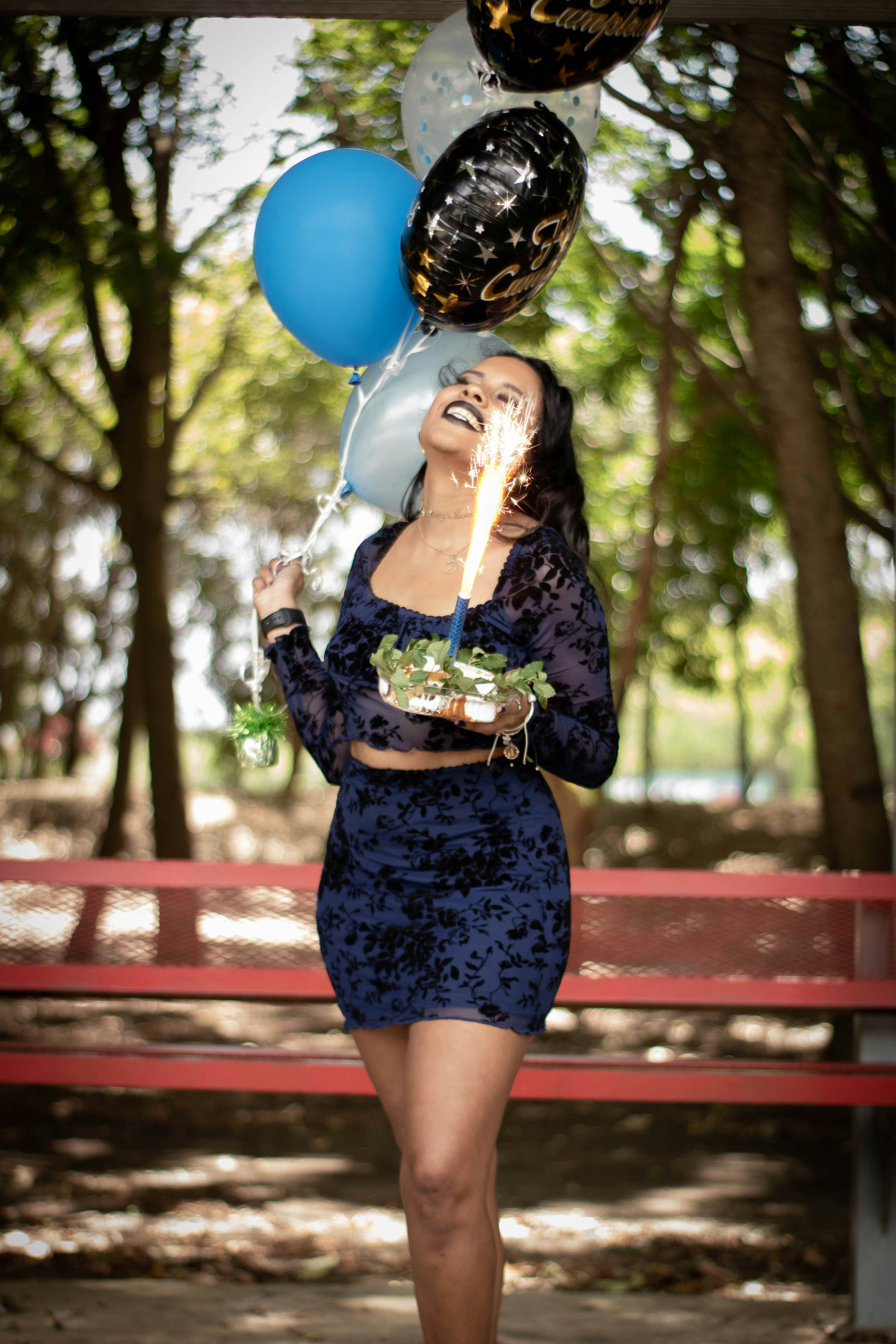 a woman in a blue dress holding balloons and a cake