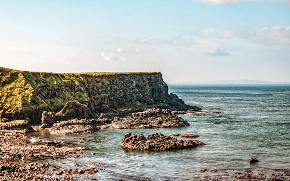 a rocky shore with a grassy cliff on the far side