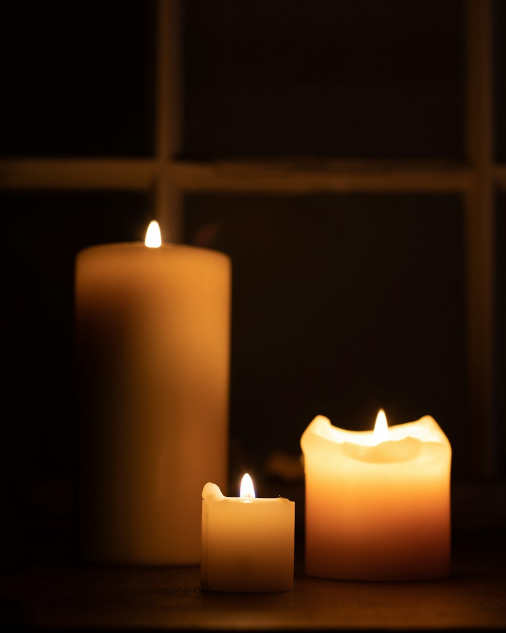 three lit candles sitting on a table in front of a window