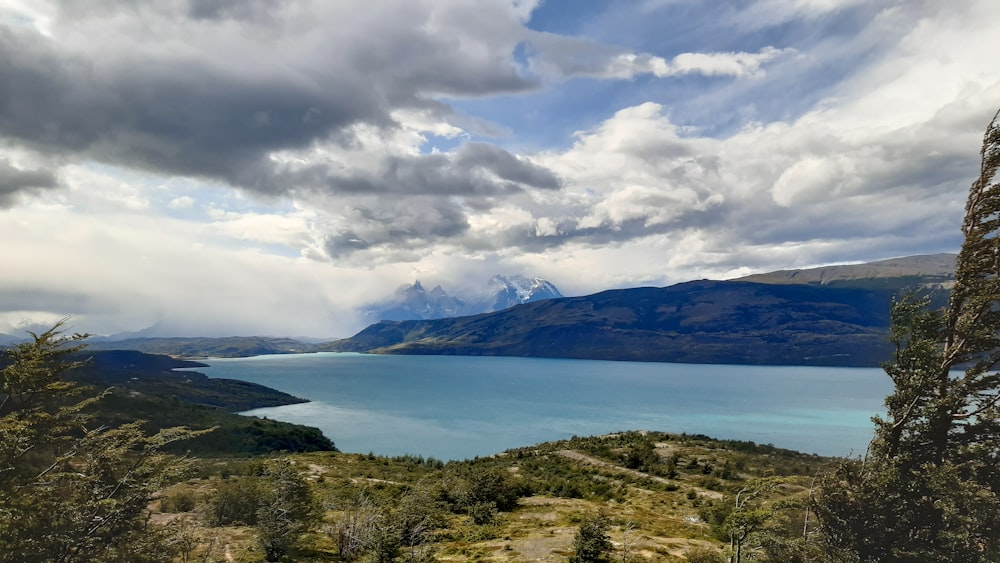 a lake surrounded by mountains under a cloudy sky