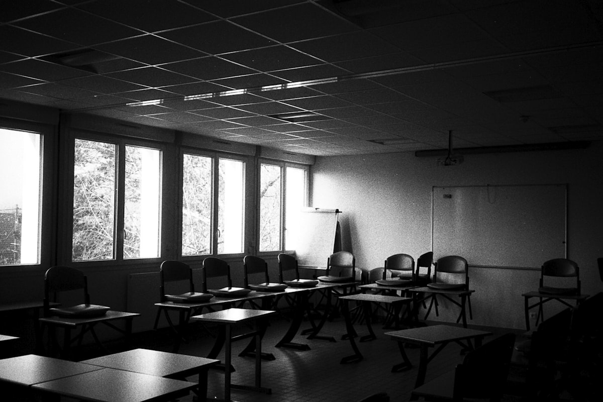 Ruang kelas kosong yang gelap dengan kursi-kursi tak terpakai, menggambarkan layanan pendidikan yang ditinggalkan