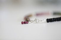 A delicate bracelet featuring small, glossy beads in a gradient of dark to light colors. The beads are linked together by a silver clasp, which lies against a softly focused, neutral background.