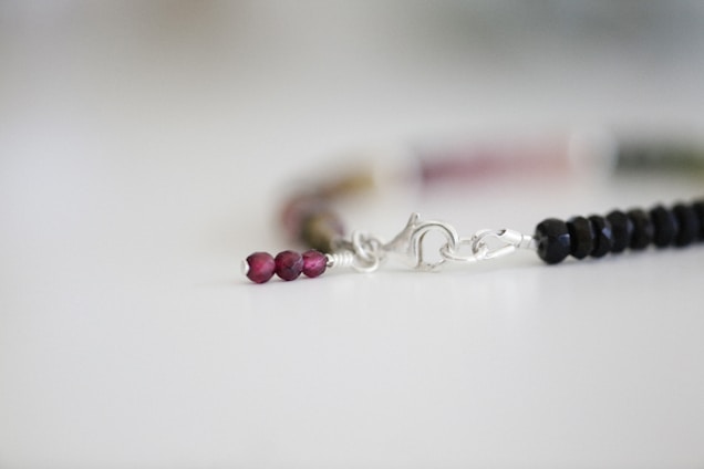 Close-up of delicate beads strung together on a minimalist bracelet resting on an ivory fabric background.