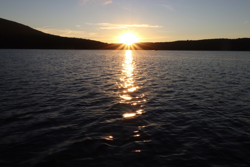 the sun is setting over a lake with mountains in the background