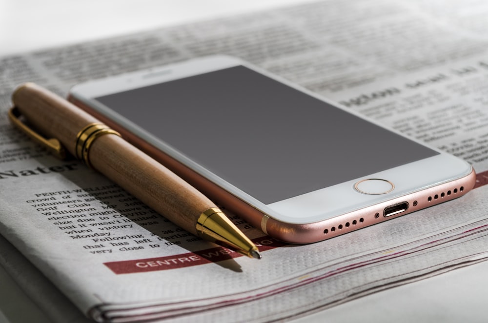 a cell phone sitting on top of a newspaper next to a pen
