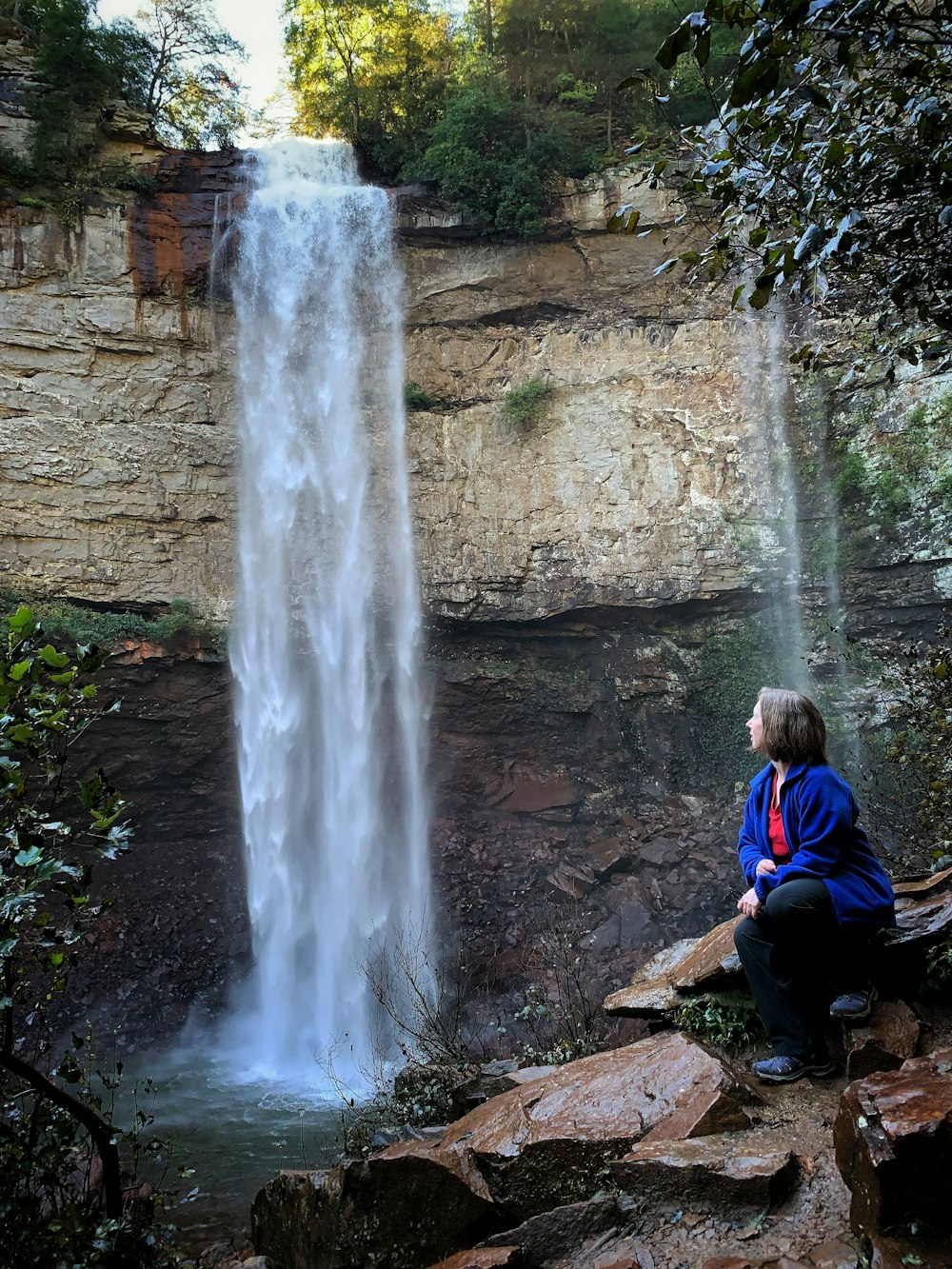 a person sitting on a rock next to a waterfall