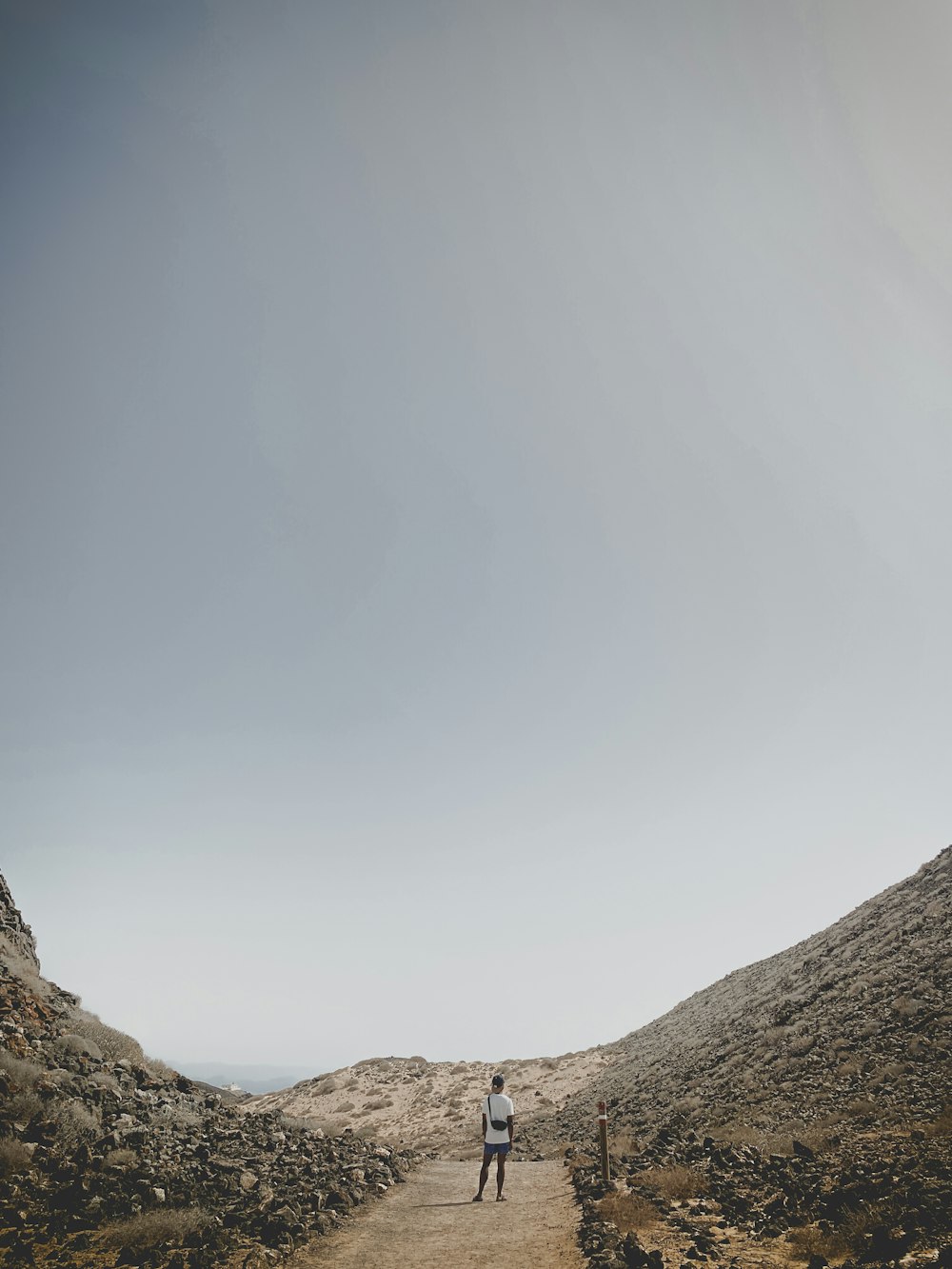 a man standing on a dirt road in the middle of a desert