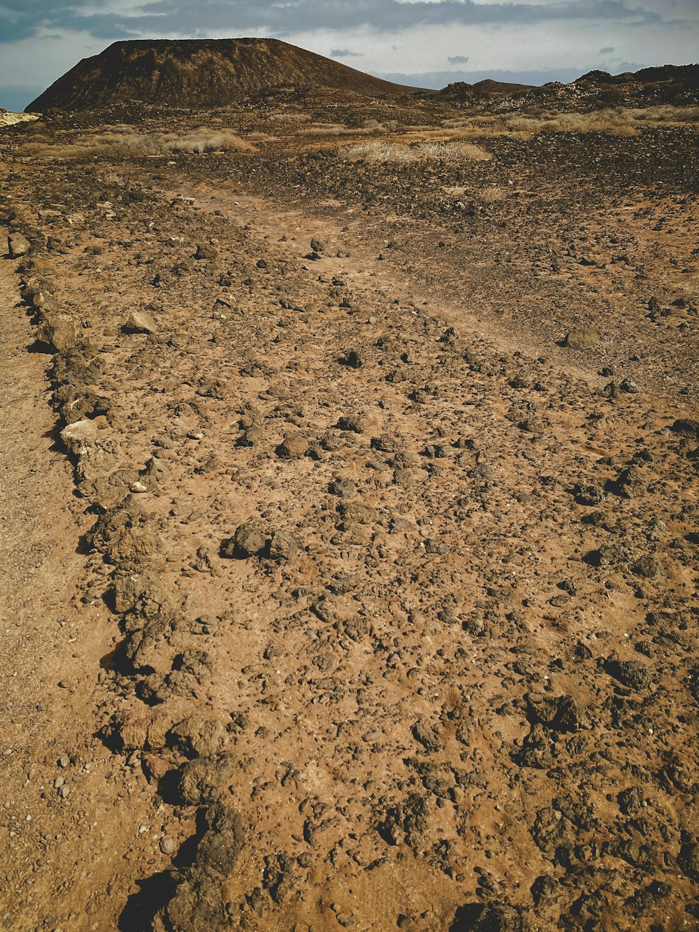 a dirt road with a hill in the background