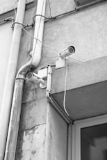 a black and white photo of a security camera attached to a building