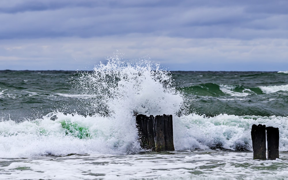 a wave crashes against a wooden post in the ocean