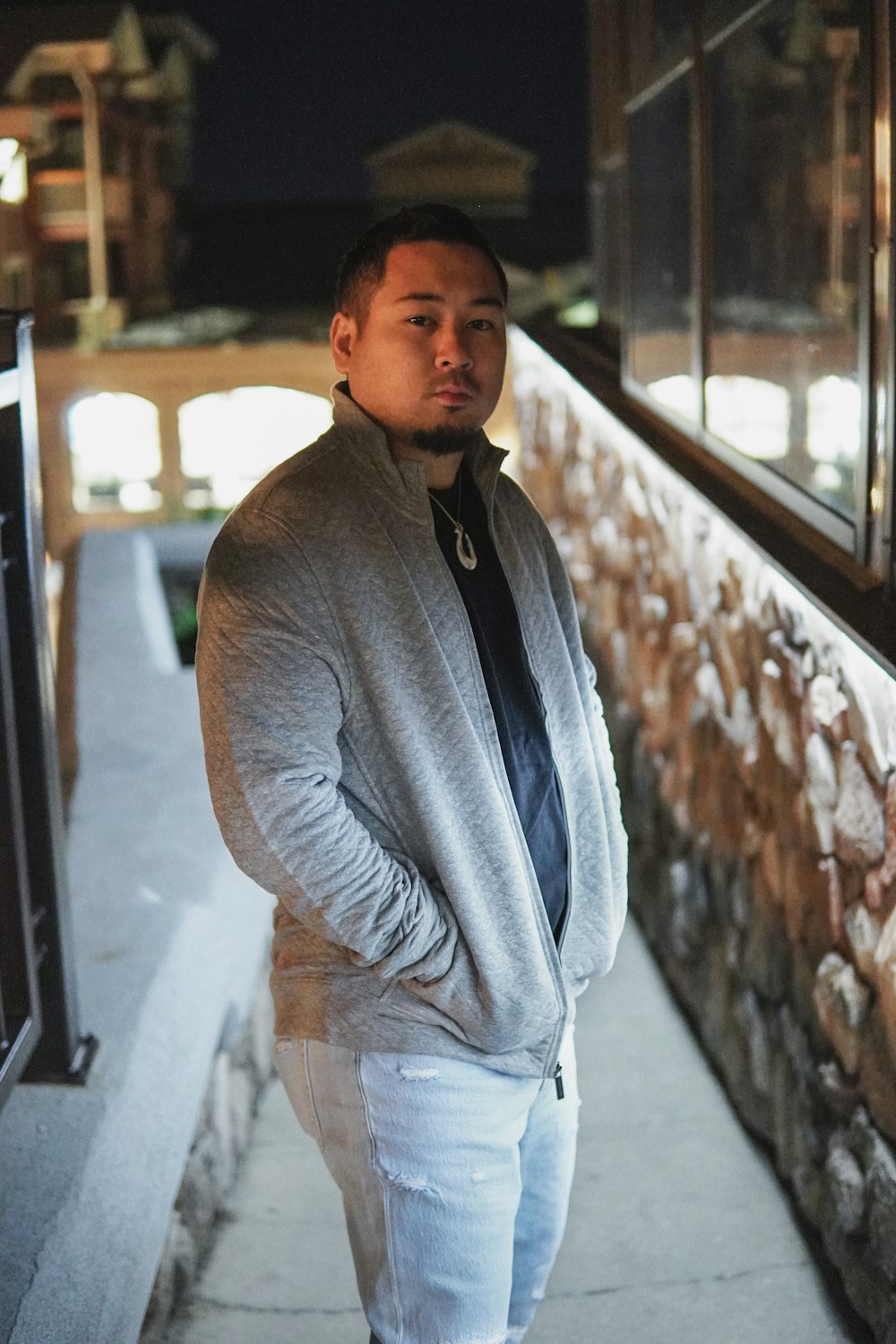 a man standing on a sidewalk next to a stone wall