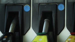 Three fuel pump nozzles are arranged in holders at a fueling station. The leftmost nozzle displays a Shell logo with 'B7', while the central nozzle is marked 'E5' with a green cap, and the right nozzle also shows 'E5' with a red cap. Blue stickers with the year 2022 are visible above each nozzle area, possibly indicating inspection stickers.