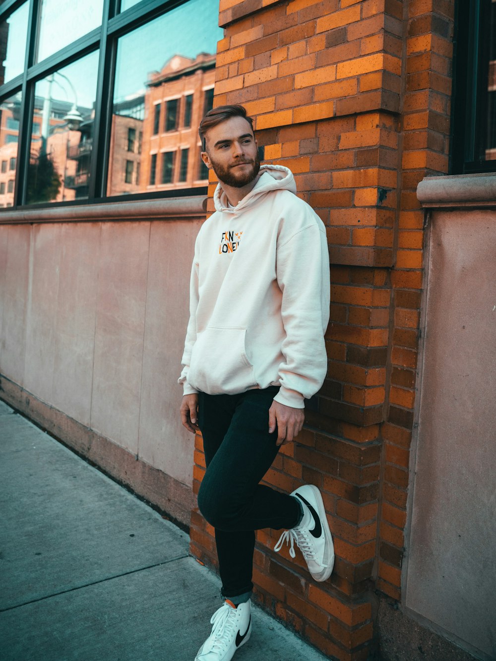 a man leaning against a brick wall wearing a white hoodie