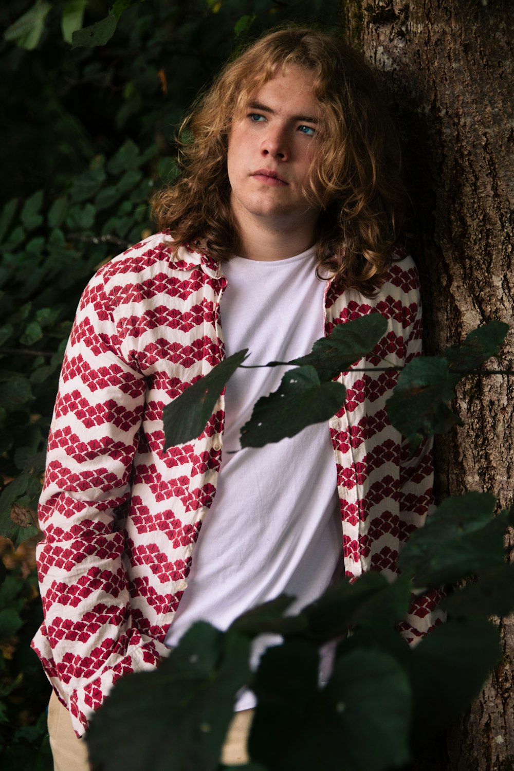 a young man leaning against a tree in a forest