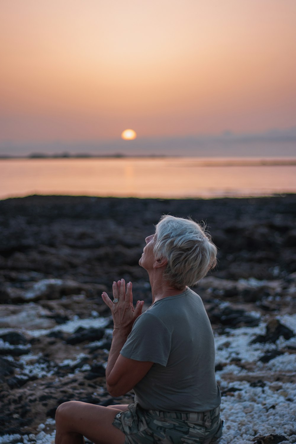 Eine Frau sitzt auf einem Felsen vor einem Gewässer
