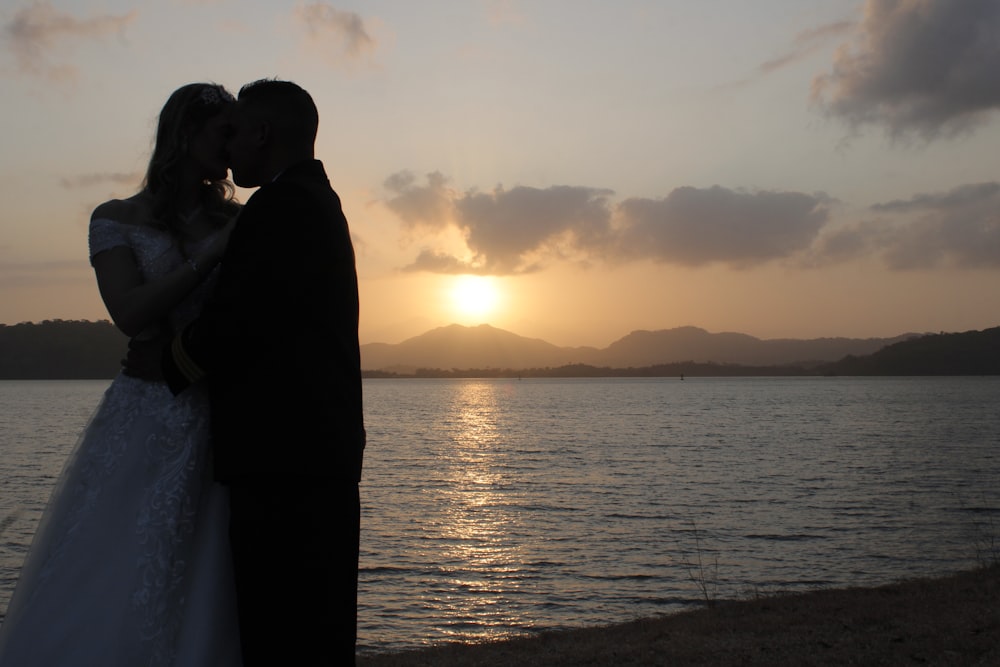 Una novia y un novio besándose frente a una puesta de sol