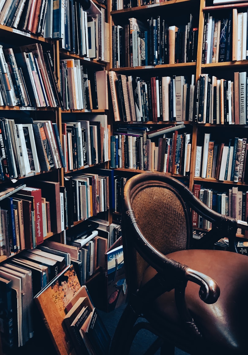A brown leather chair surrounded by bookshelves, piled high with books.