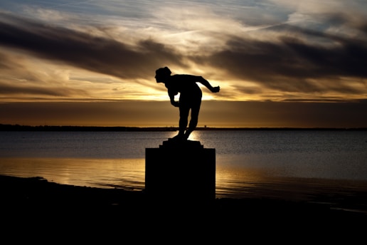 a statue of a man is silhouetted against a sunset