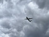 An airplane is flying upwards against a backdrop of thick, gray, and overcast clouds, indicating possible stormy weather.