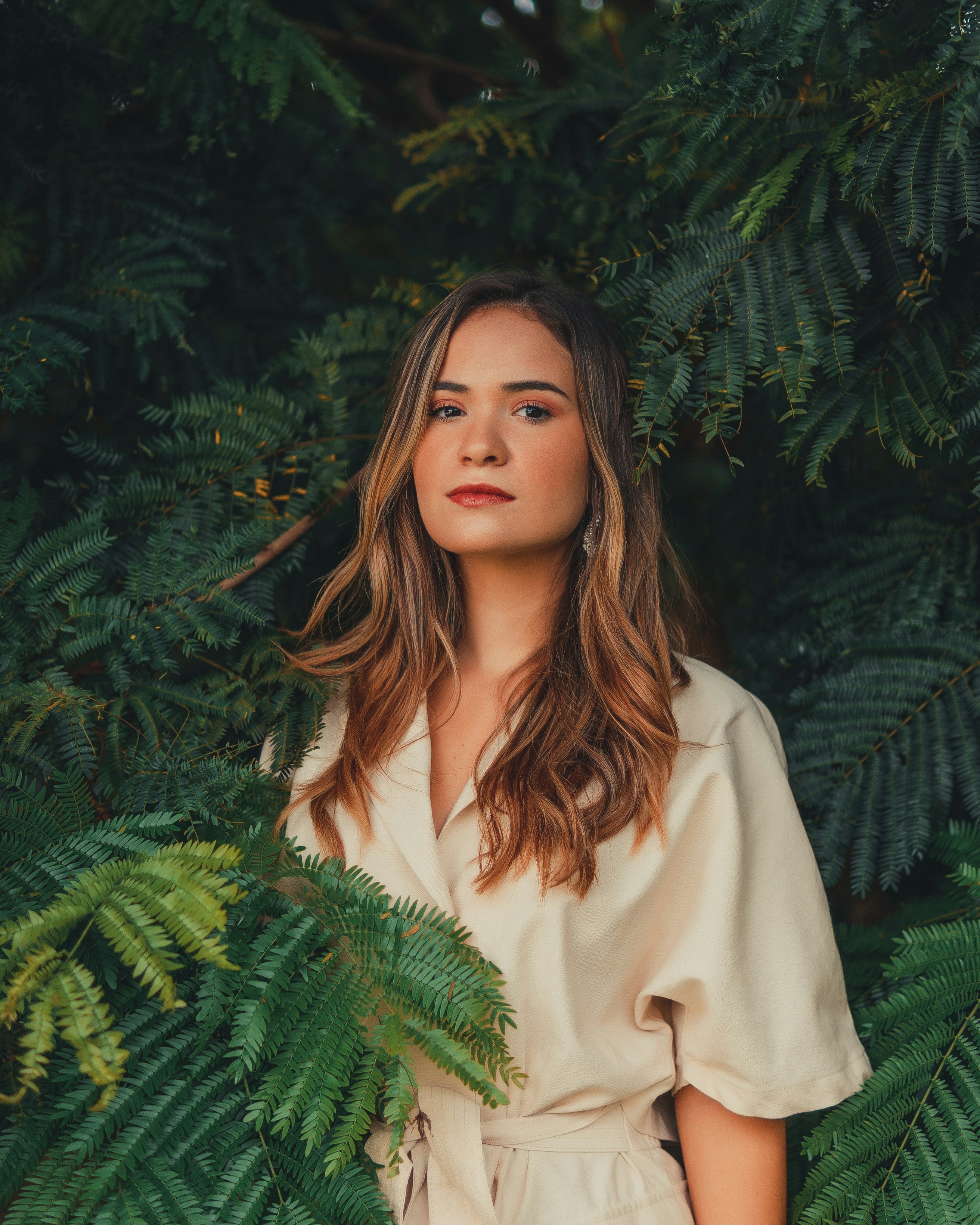 Young woman in a cream jumpsuit among lush green foliage