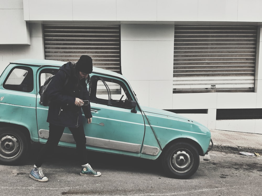 a man standing next to a small blue car