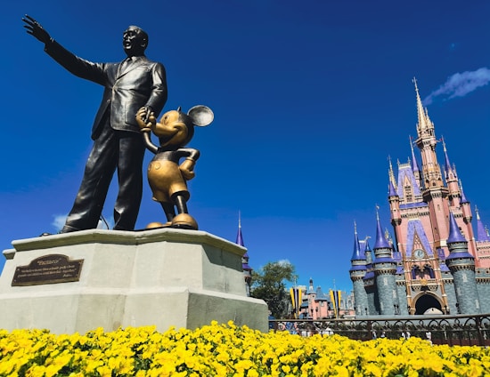 a statue of walt and mickey mouse in front of a castle