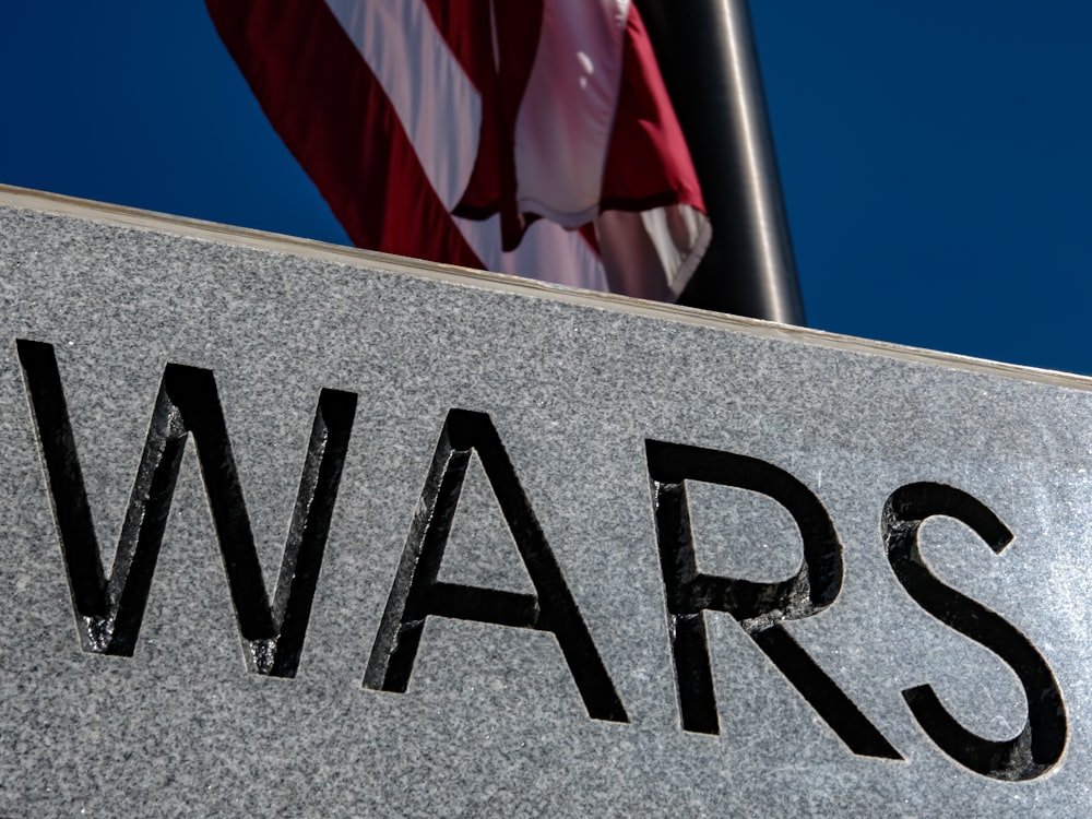 a close up of a sign with a flag in the background