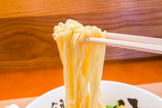 Close-up of hands holding beautifully crafted bamboo chopsticks over a rustic wooden table with leafy greens in the background.