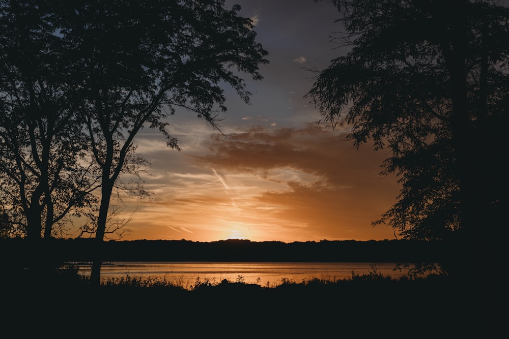 the sun is setting over a lake with trees