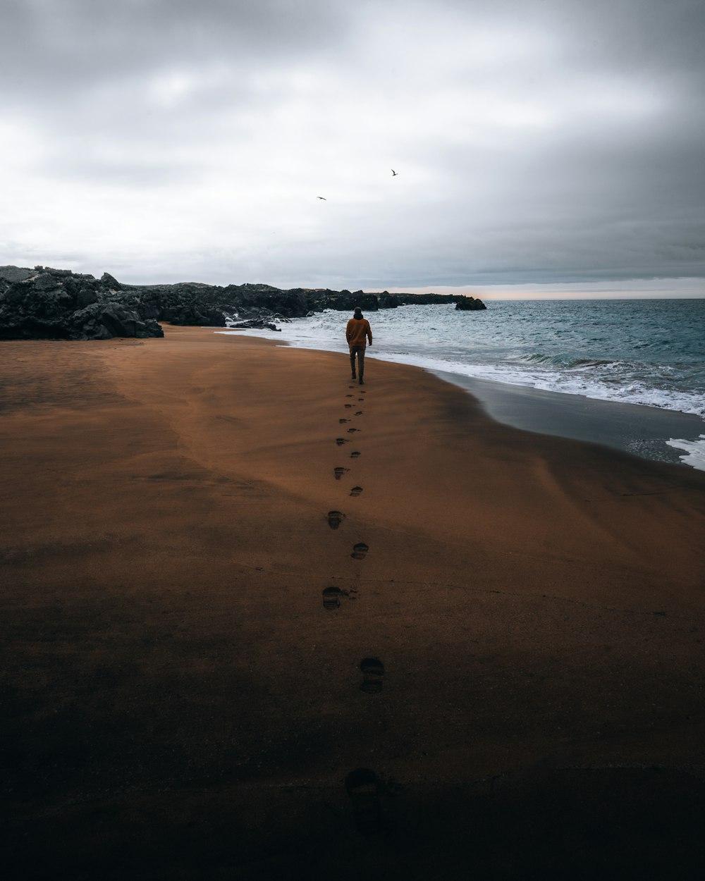 Eine Person, die an einem Strand mit Fußabdrücken im Sand spazieren geht