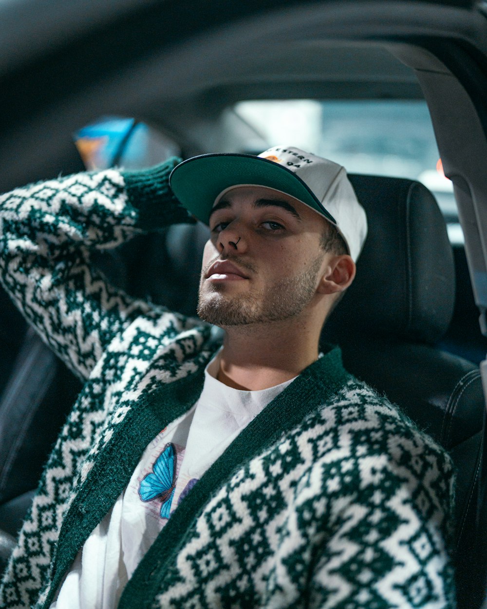 a man sitting in a car wearing a green and white sweater