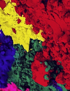 A vibrant mixture of colorful powdered pigments including red, yellow, green, blue, and pink, creating a textured and visually striking composition.